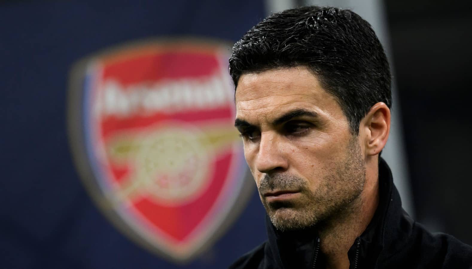 Arsenal manager Mikel Arteta standing in front of the Arsenal club crest